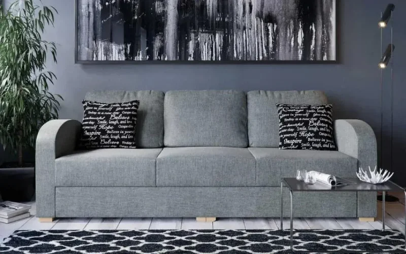 A modern, grey fabric 3 seater sofa with curved armrests and a tufted design.